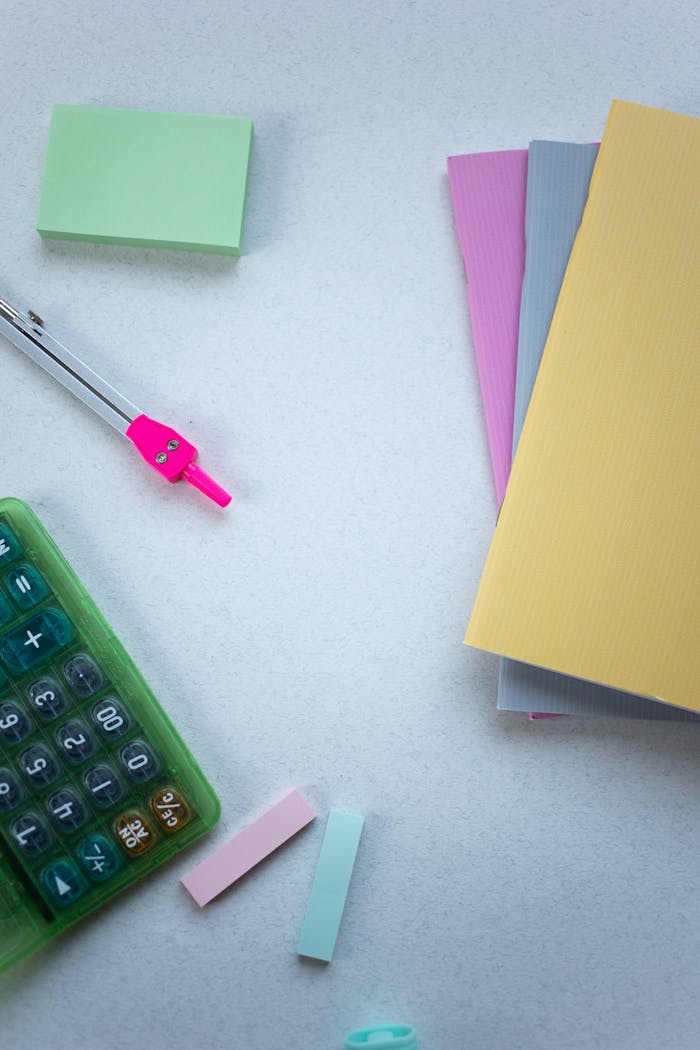 Flat lay of colorful stationery items with calculator and notepads on a white background.
