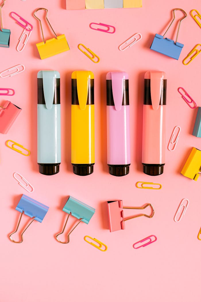 An arrangement of vibrant markers and clips on a pink backdrop, perfect for office themes.